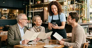 Servicekraft bedient Gäste im Restaurant mit digitaler Kassensoftware und mobiler Bestellaufnahme.
