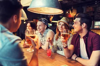 Fuenf junge Gaeste sitzen an einem Tisch und trinken Bier.