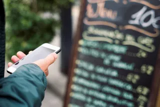 Ein Gast steht vor eine Gastronomie mit Smartphone
