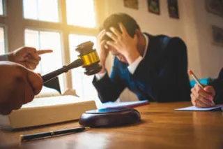 Ein verzweifelter Mann in Anzug sitzt vor Gericht und im Vordergrund wird ein Hammer geschlagen