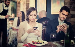 Ein Paar sitzt in einer Gastronomie und hat nur Augen fürs Handy