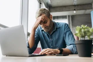 Ein Mann sitzt vor dem Laptop und hat seinen Kopf verzweifelt auf der Hand gestützt.