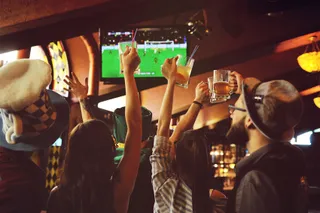 Gaeste jubeln in einer Bar vor dem Fernseher