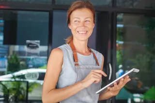 Kellnerin mit iPad steht vor einer Gastronomie