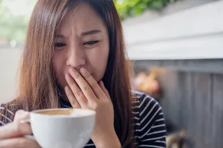 Junge Frau hält sich ihre Hand angeeckelt vor den Mund und hält ihren Kaffe von sich weg.